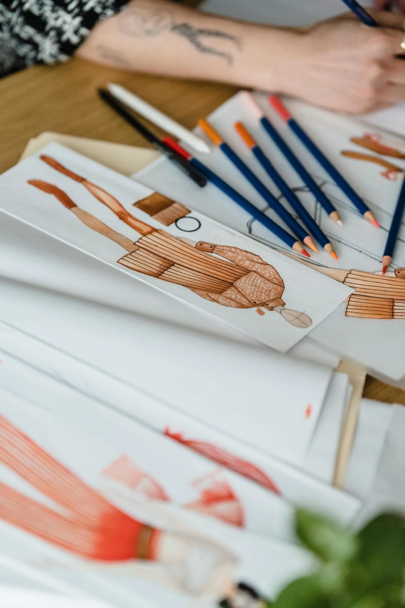 Artist's desk with fashion illustration sketches and coloured pencils mid-drawing