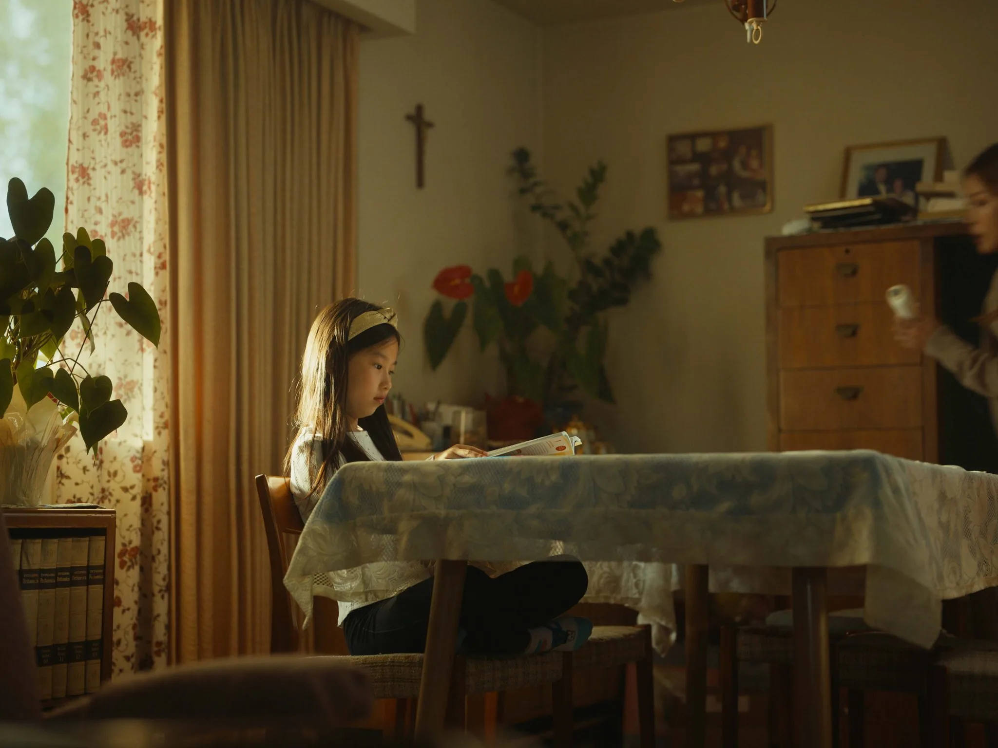 Cinematic film still of a young girl reading at a dining table in warm window light, for the Introduction to Filmmaking workshop
