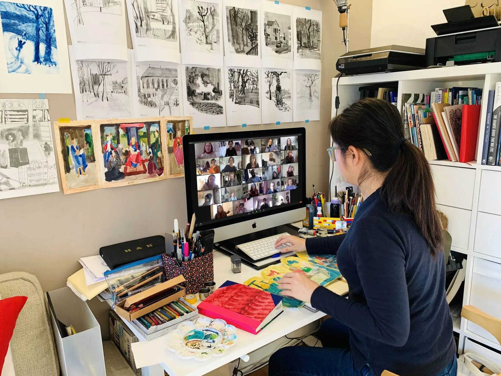 Illustrator on a group video call at her desk, surrounded by sketches and watercolour artwork pinned to the wall