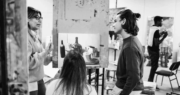 Black-and-white photo of an instructor critiquing a student's still-life painting during a studio art class