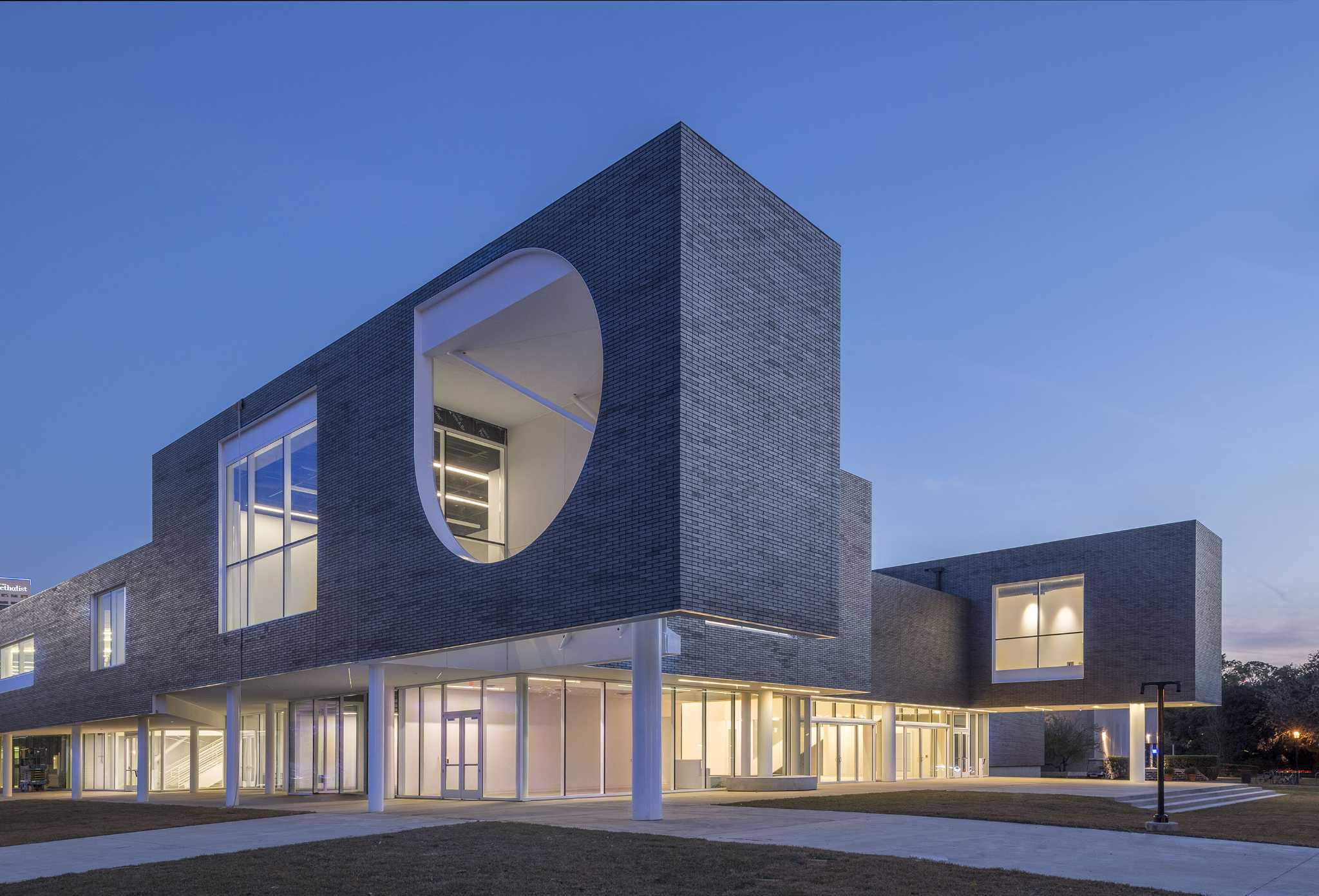 Modern brick arts building with a large circular cutout window glowing at dusk on a university campus