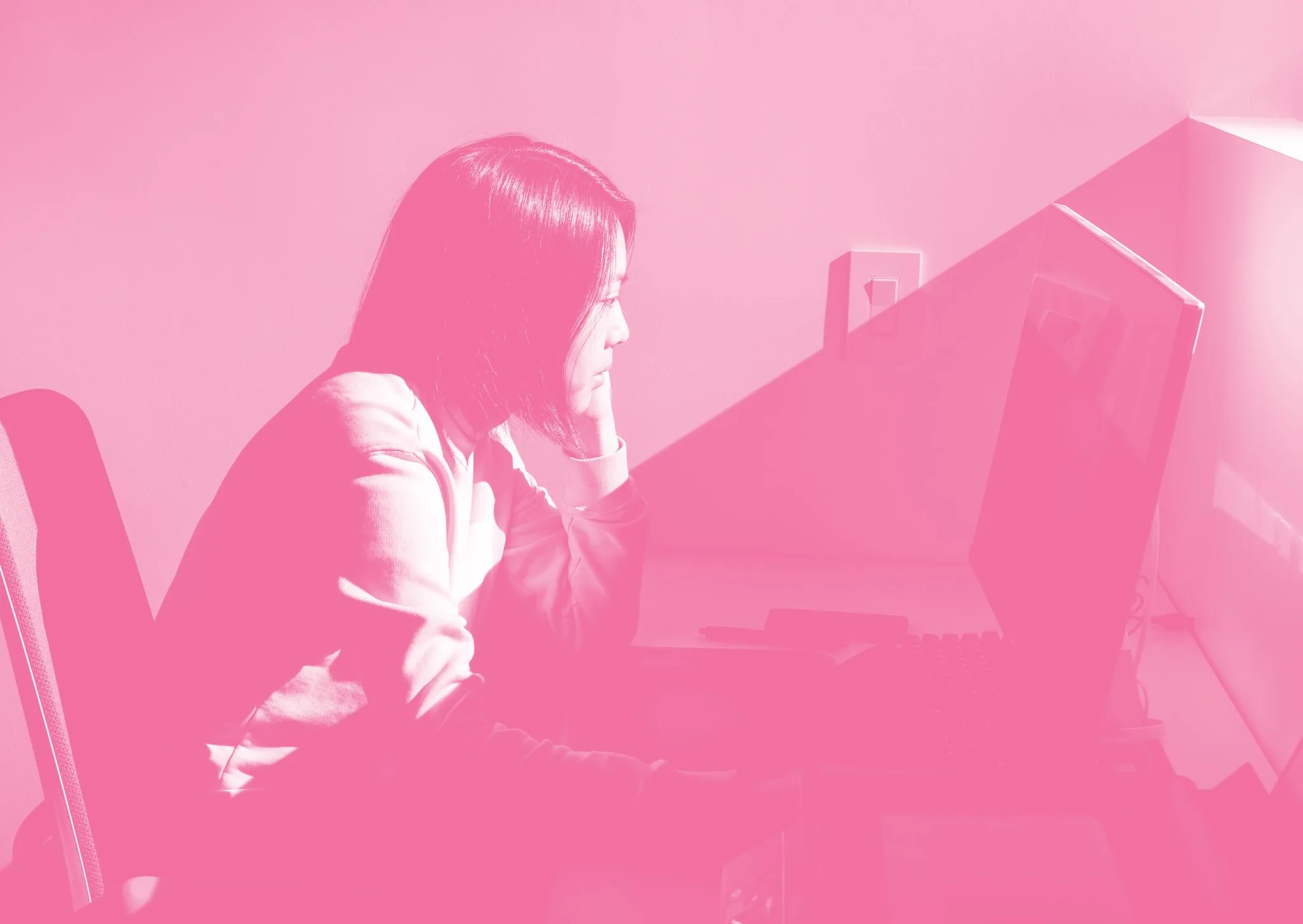 Pink duotone photo of a student studying intently at a desktop computer