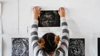 Student pinning dark monoprint portraits onto a white studio wall