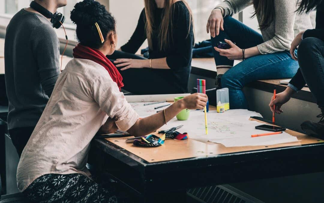 Group of students brainstorming around a table covered with paper, markers and phones
