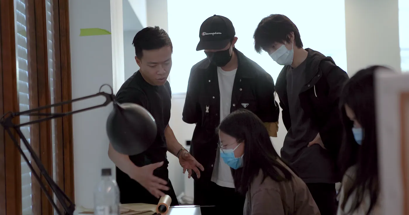 A group huddled around a shared project in the studio